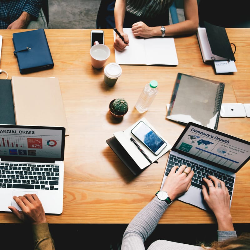 Overhead view of a B2B marketing team around a meeting table with laptops showing growth and performance charts, comparing options while choosing the best SEO agency for B2B
